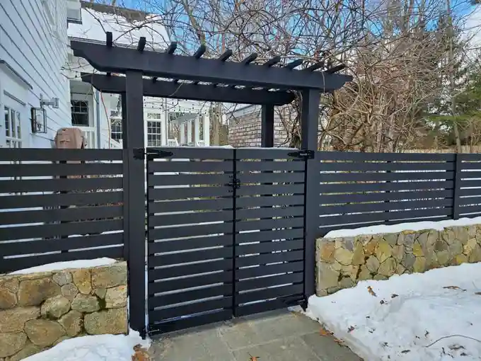 Black horizontal-slat fence with a matching pergola-topped entry gate over a bluestone path
