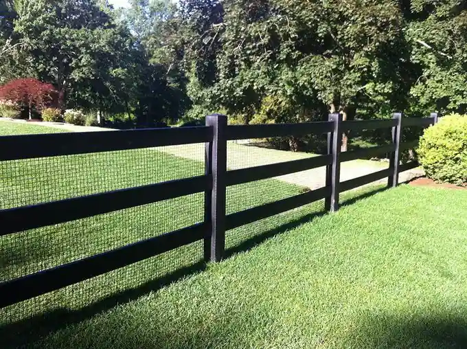 Black three-board paddock-style fence with wire backing across a lawn