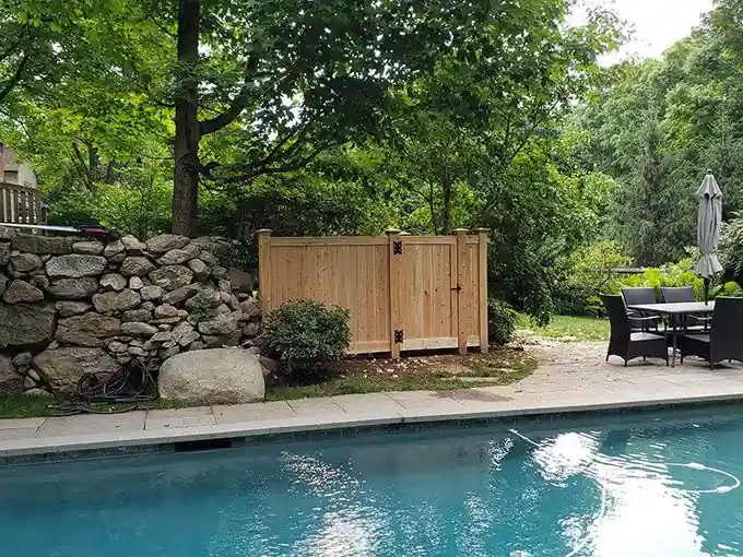 Cedar board equipment enclosure beside an in-ground pool and stone wall