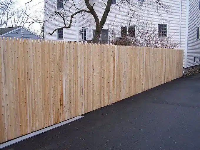 Tall cedar stockade privacy fence along a driveway beside a white house