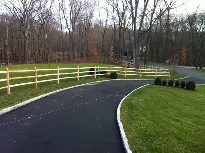 Natural post-and-rail fence following a curved asphalt driveway