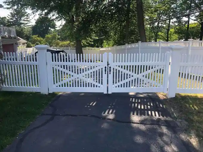 White picket double driveway gate with X-bracing across an asphalt drive