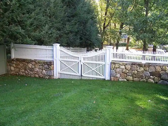 White picket fence and X-brace double gate set on top of a fieldstone wall