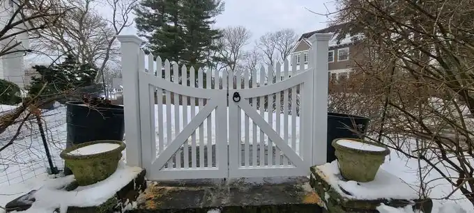 White scalloped picket double gate between square posts, planters either side