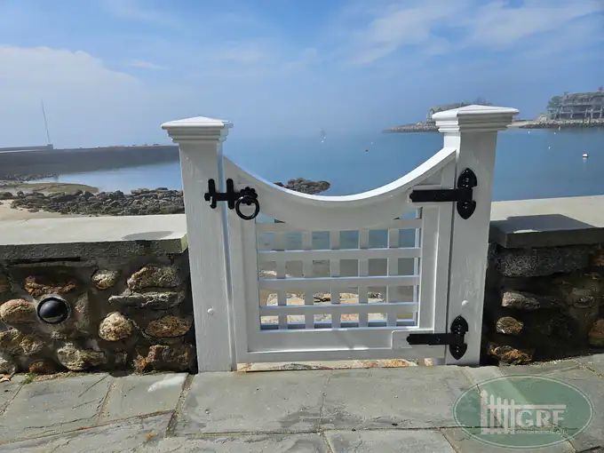 Custom white wave-top picket gate with lattice infill on a waterfront stone wall