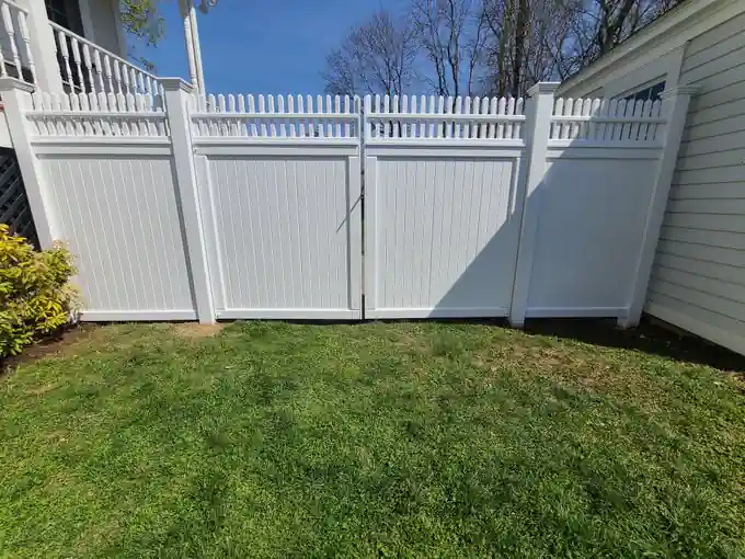 White vinyl picket-top privacy fence with a double gate beside a porch