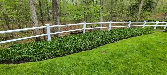 White vinyl two-rail ranch fence along a mulched hedge border