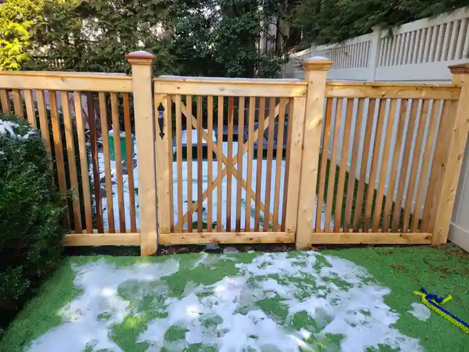 Natural cedar picket fence with an arched arbor gate and diagonal cross-brace, snow on the ground
