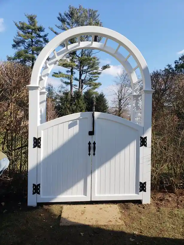 White vinyl arched arbor gate with decorative wrought-iron strap hinges and handles